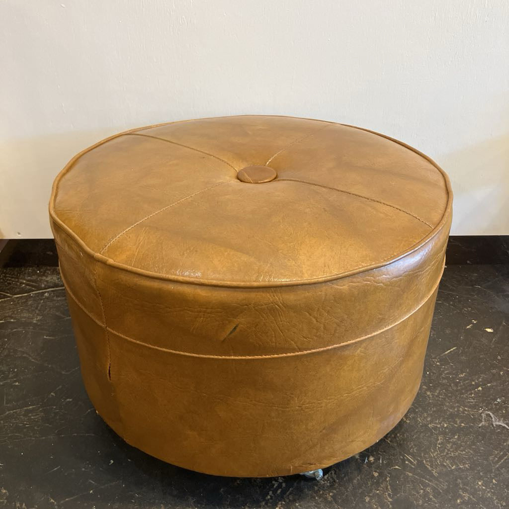 Brown leather ottoman on a black floor with a white wall background