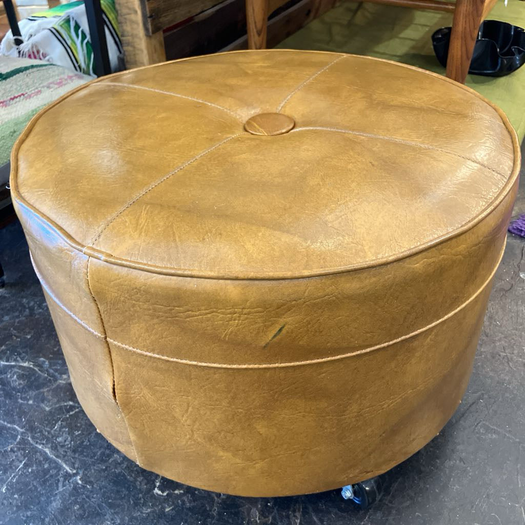 Round brown leather ottoman on wheels in a room setting.