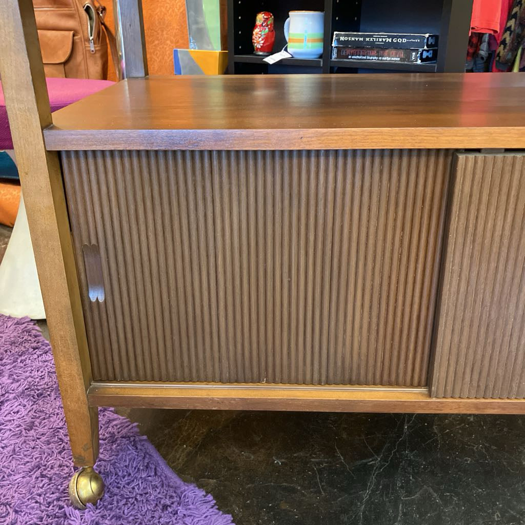 Wooden cabinet with ribbed design on a black floor with a purple rug.