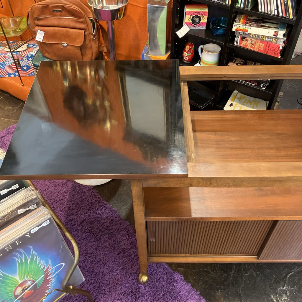 Wooden desk with a reflective surface, books, and a lamp in a room setting.