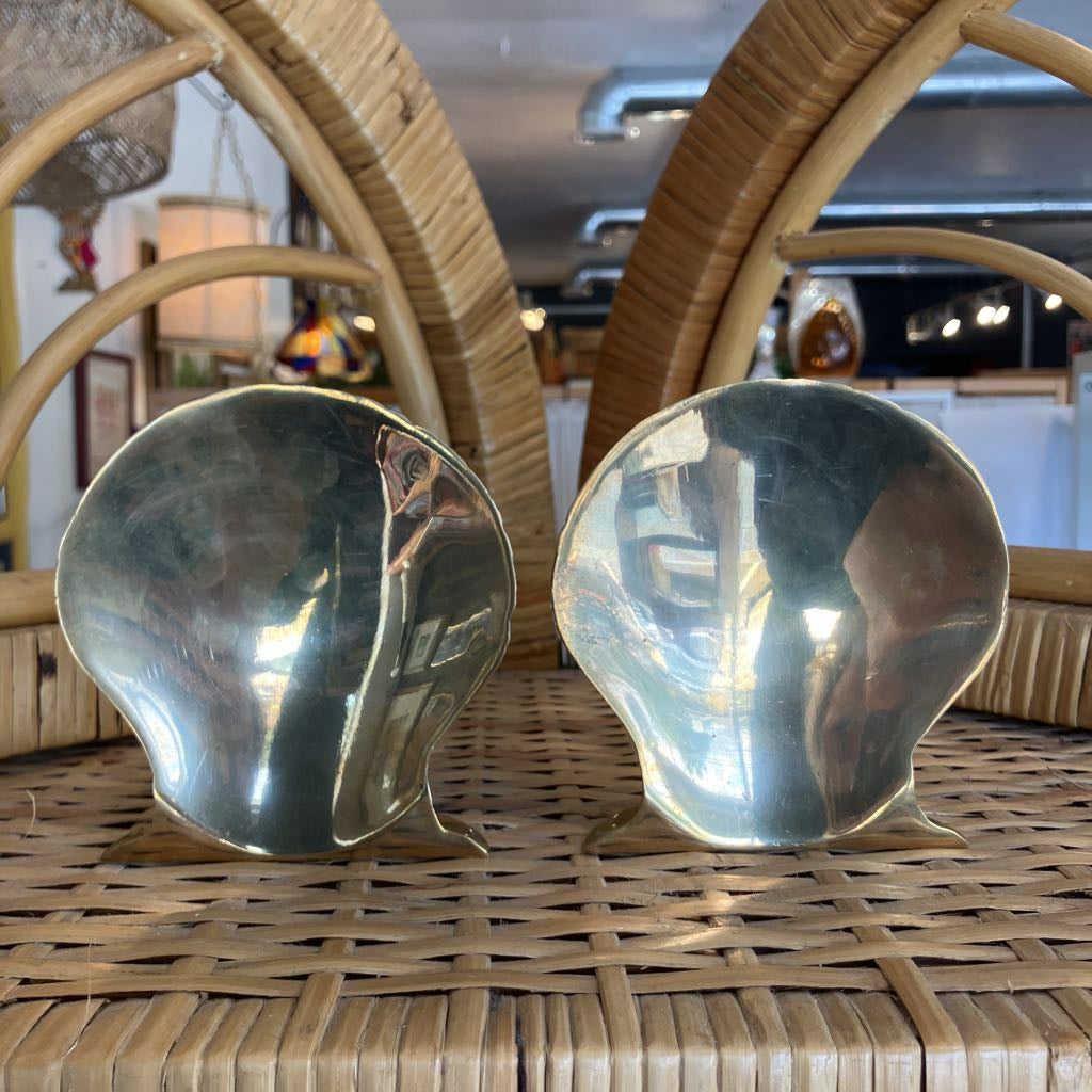 Two metallic shell-shaped objects on a woven surface with blurred indoor background