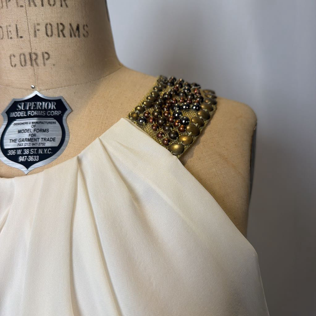 Mannequin wearing a draped garment with a decorative shoulder piece on a plain background