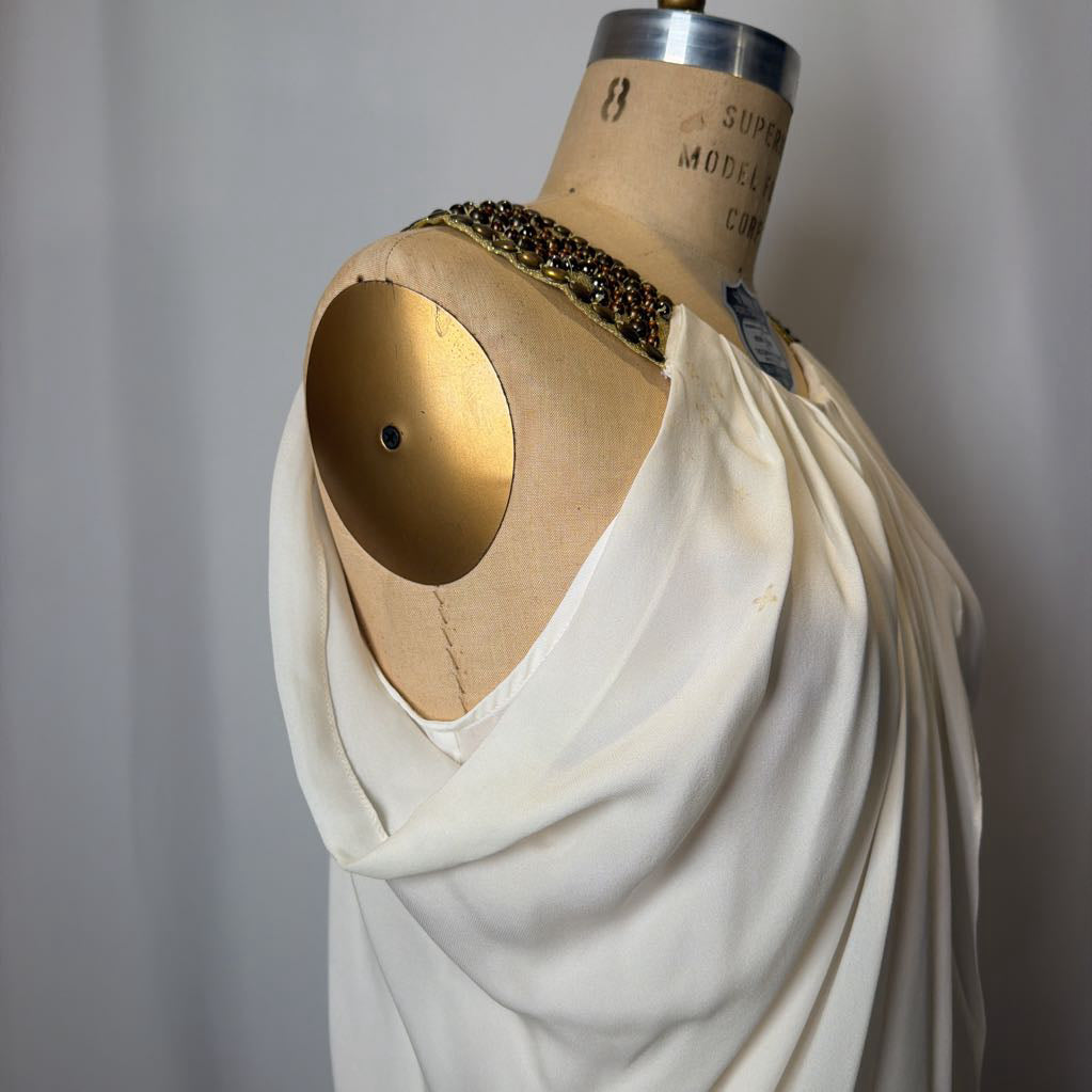 Mannequin wearing a white garment with a gold circular detail on a plain background