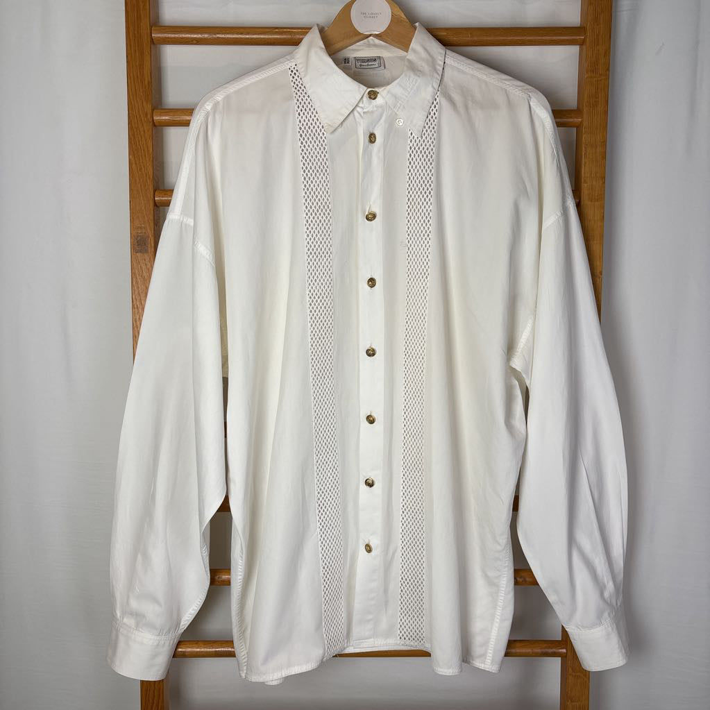 A white long sleeve shirt with mesh panels hanging on a wooden rack.