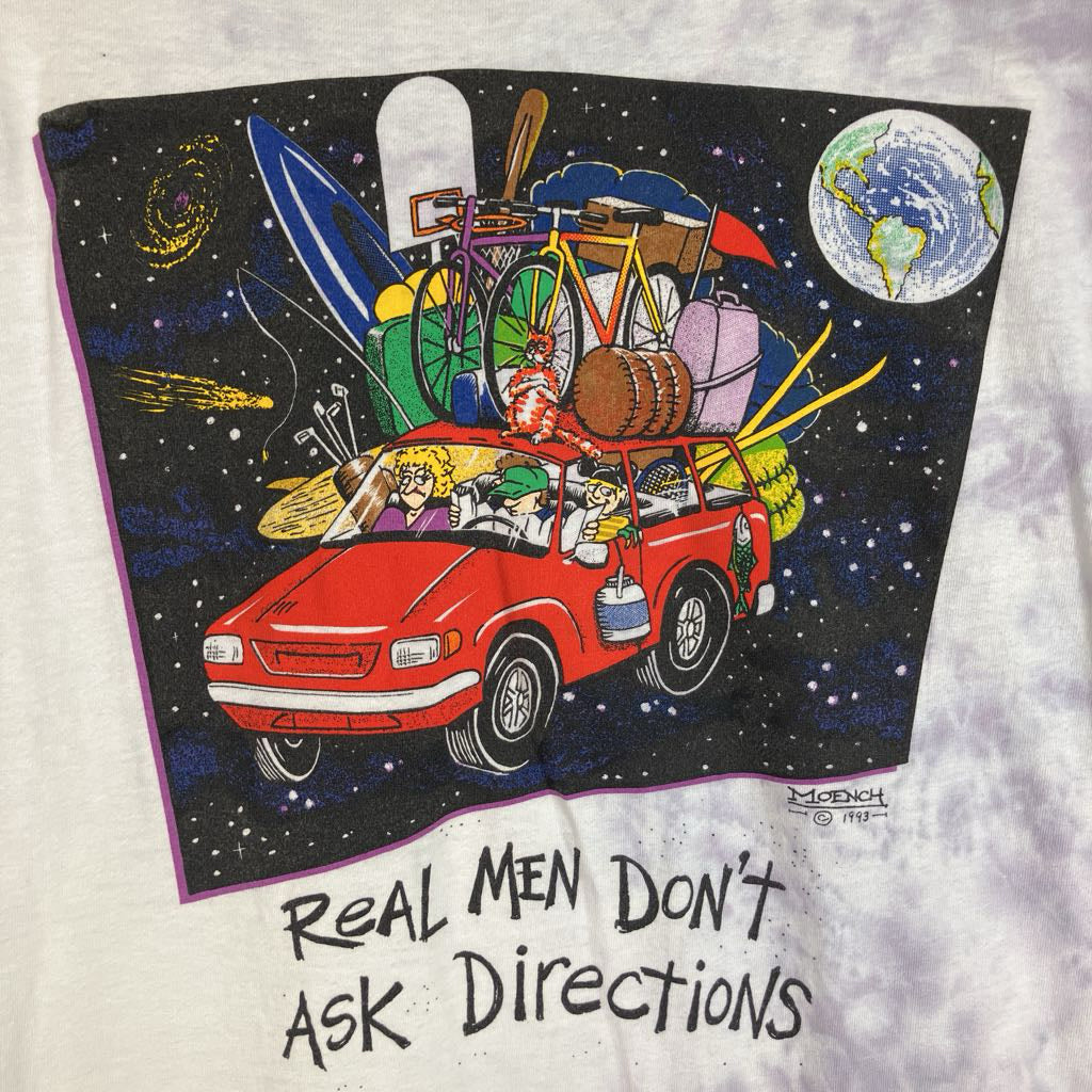 A vintage tie-dye graphic t-shirt featuring a cartoon illustration of a red car packed with travel items in outer space, with the text 'REAL MEN DON'T ASK DIRECTIONS' printed below.