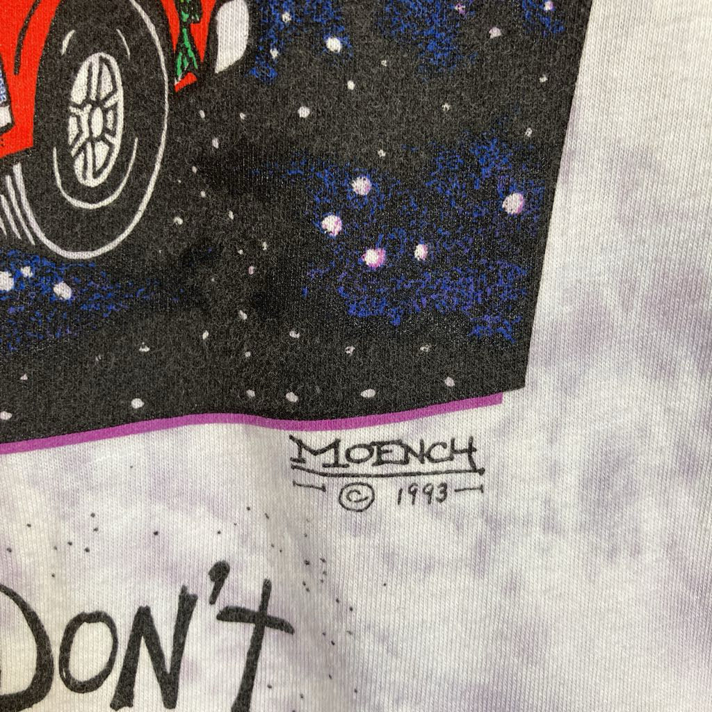 Close-up of a vintage graphic t-shirt featuring a black space print with a red car wheel, blue starry nebula, and a Moench copyright 1993 signature on a white tie-dye fabric.