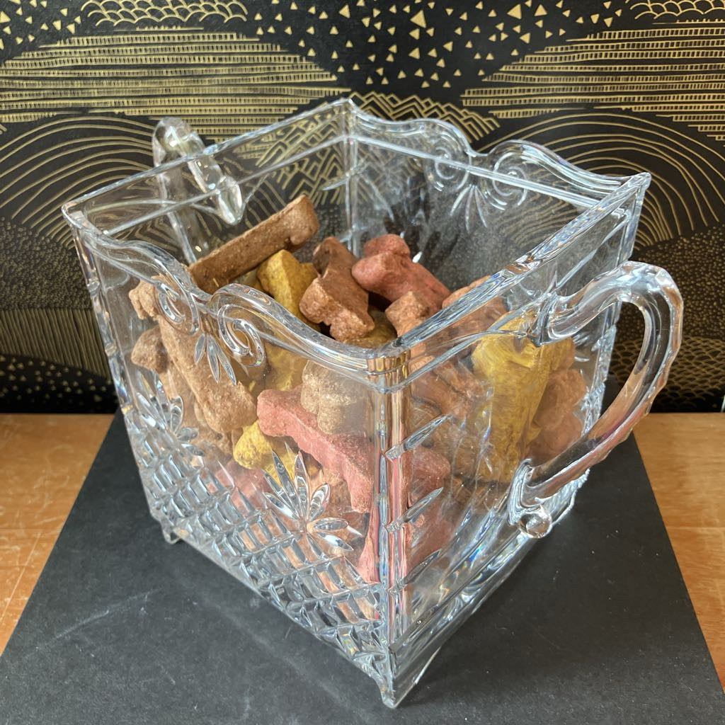 Clear glass container filled with dog treats on a black surface with a gold patterned background.