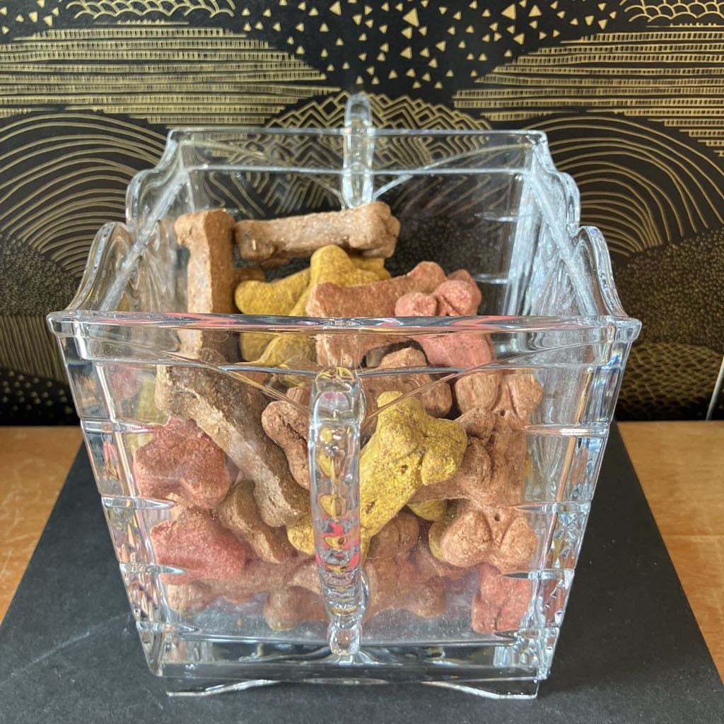 Clear glass container filled with colorful dog treats on a dark surface.