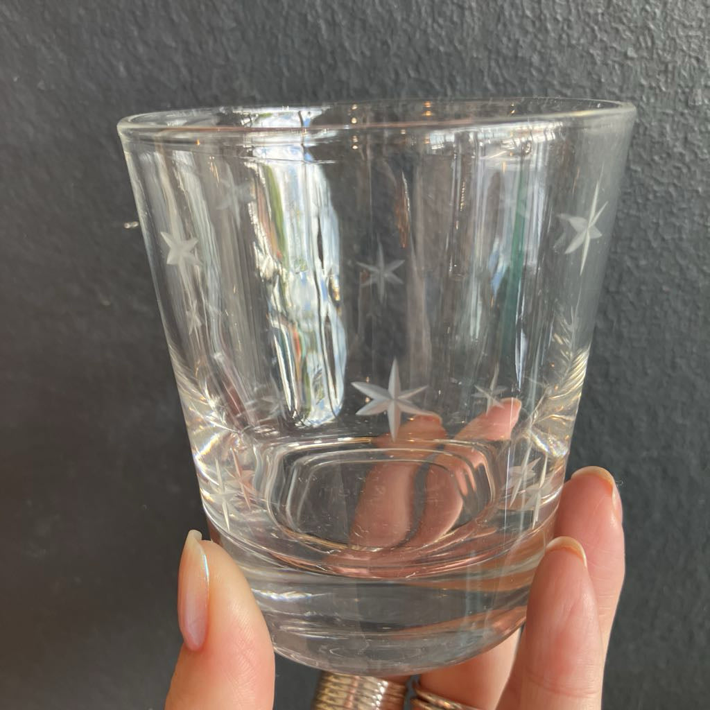 A clear glass tumbler with etched star patterns, held by a hand against a dark textured wall.