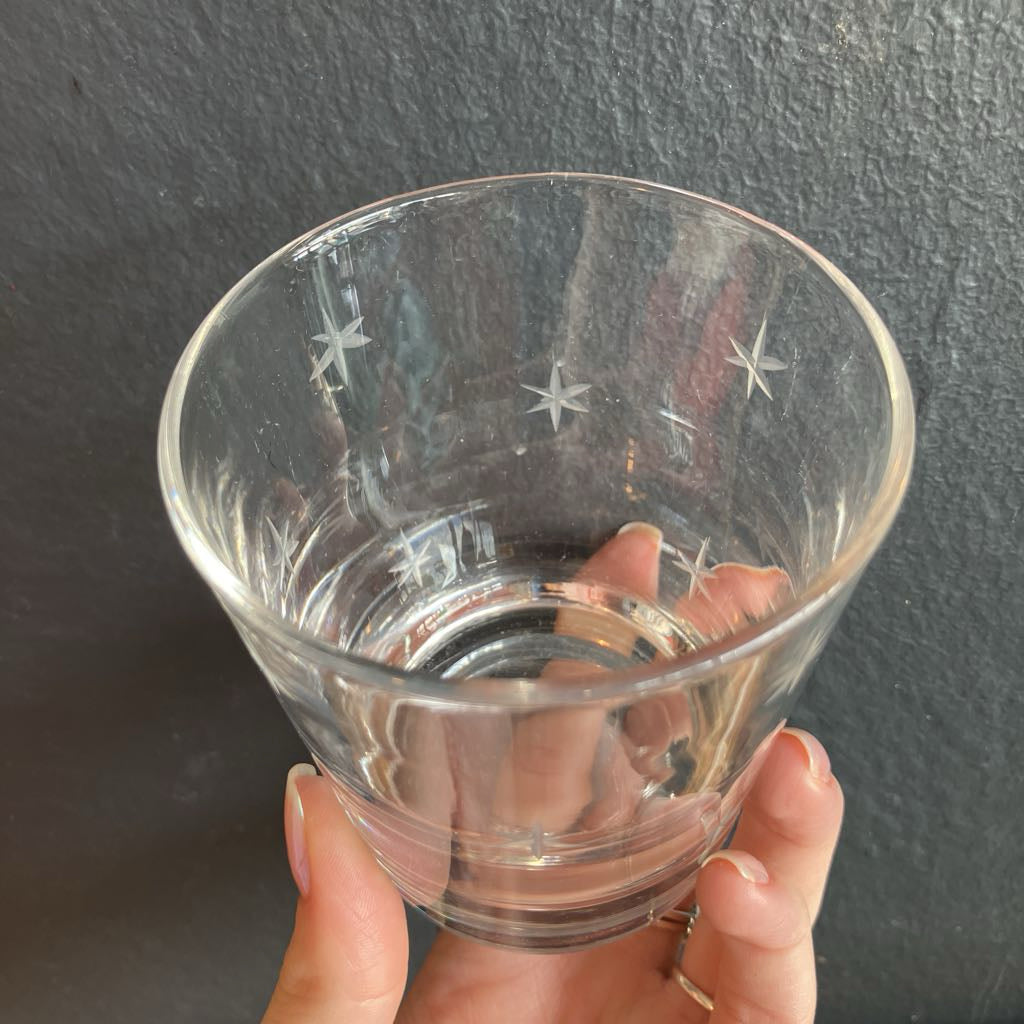 A hand holding a clear glass tumbler with etched star patterns, set against a dark textured background.