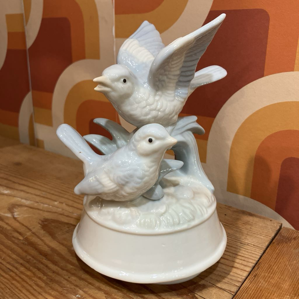 White ceramic birds on a decorative base against an orange and brown patterned wall.