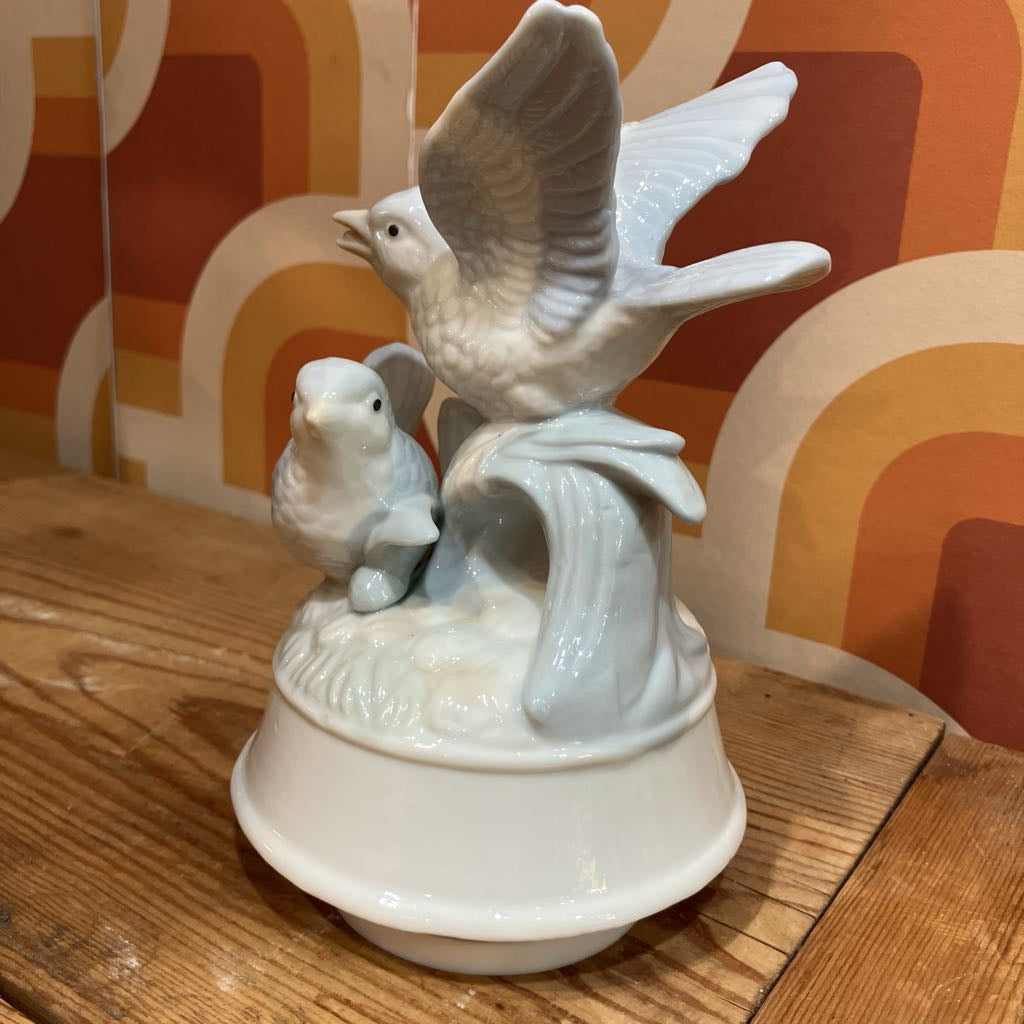 Ceramic bird figurine on a wooden surface with a colorful abstract pattern in the background