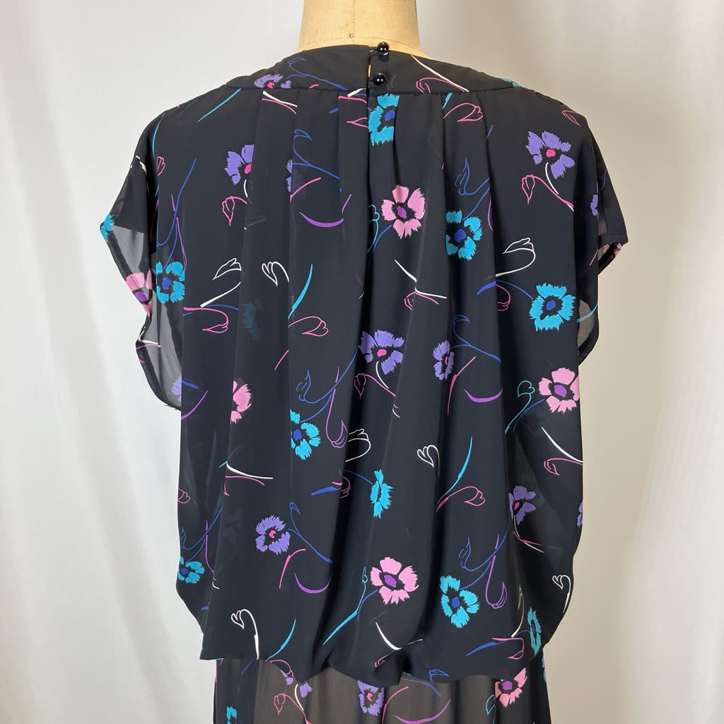 Black blouse with colorful floral pattern on a mannequin against a plain background