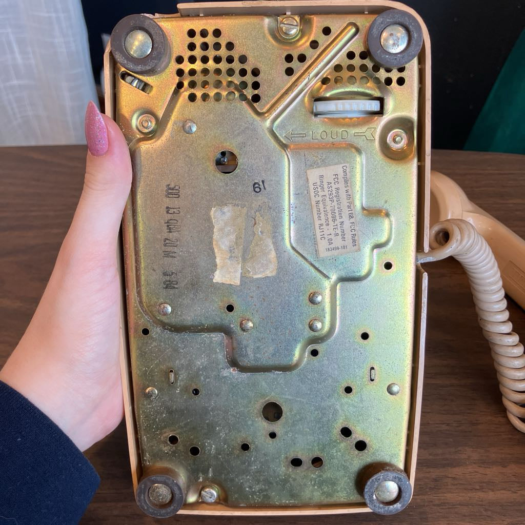 Vintage phone with a worn-out back panel held by a hand on a wooden surface.