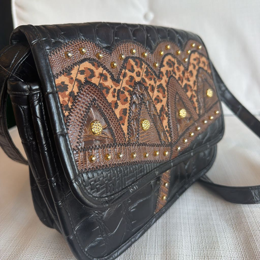 Black leather handbag with leopard print and gold studs on a light background