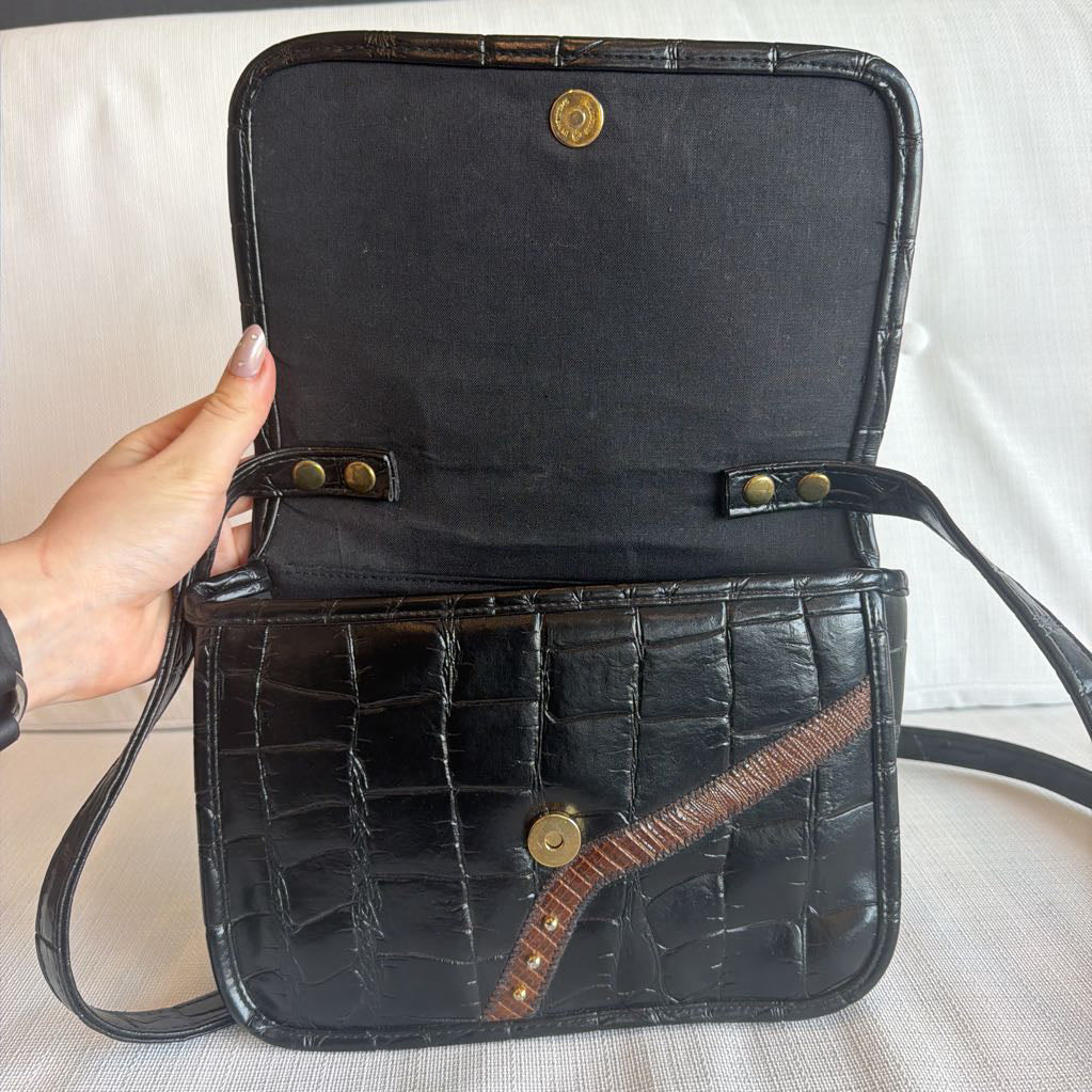 Black crocodile skin handbag with gold buttons held by a hand on a light background