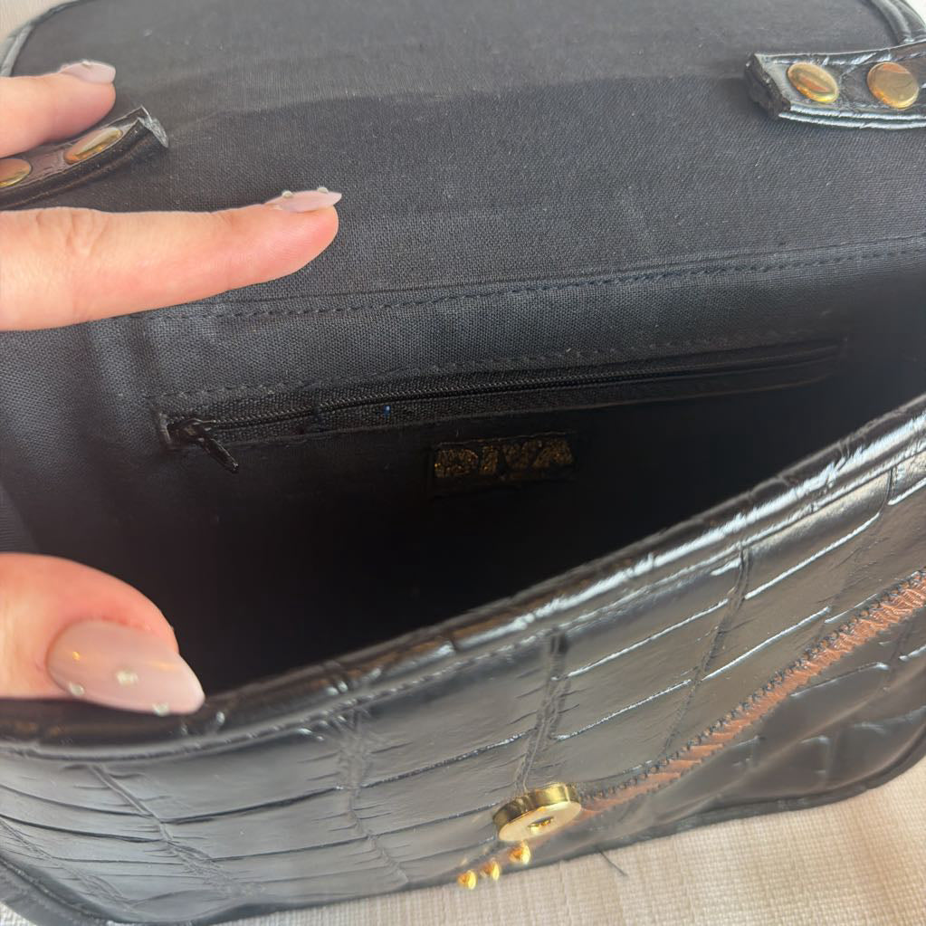 Close-up of a hand holding a black textured bag with gold accents.