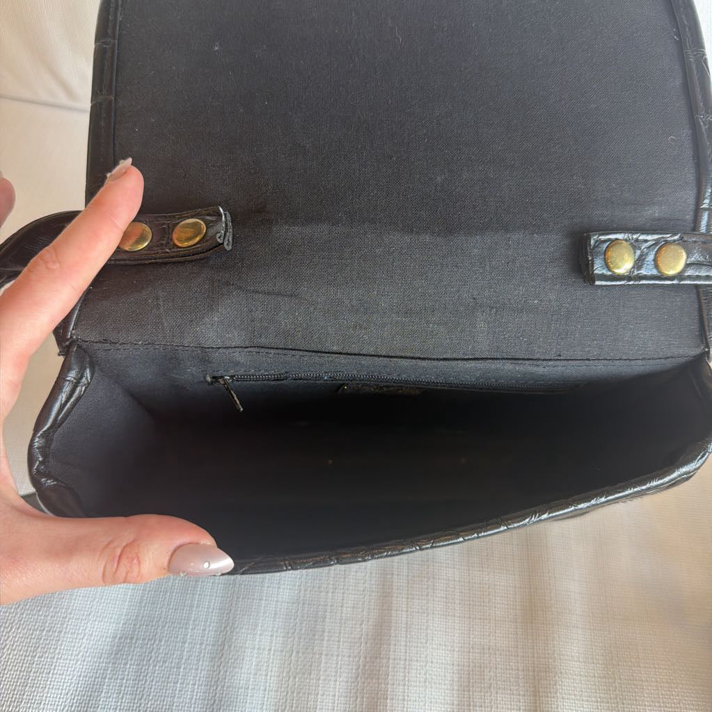Black handbag with gold hardware held by a hand on a neutral background