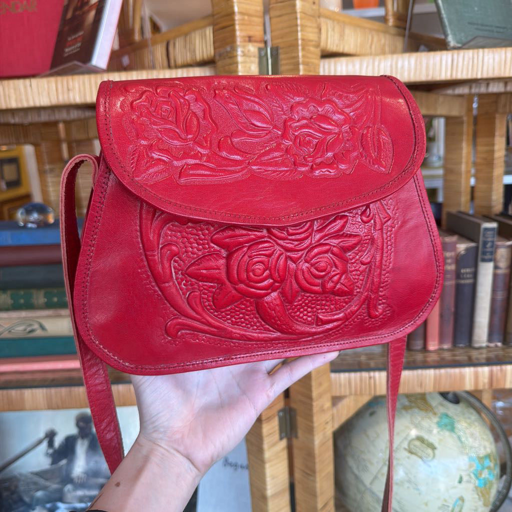 Red leather handbag with intricate designs held in front of a bookshelf.