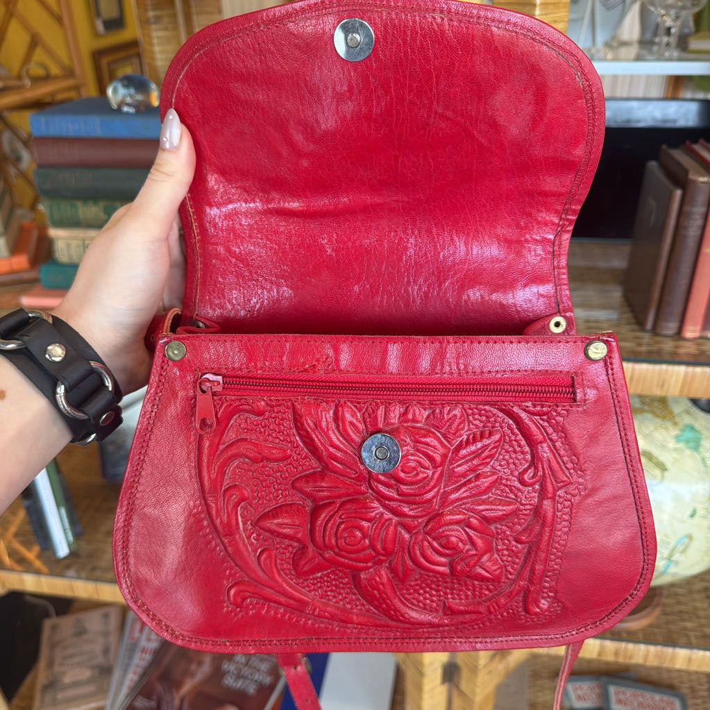 Red leather wallet with floral embossing held by a person in a blurred indoor setting.