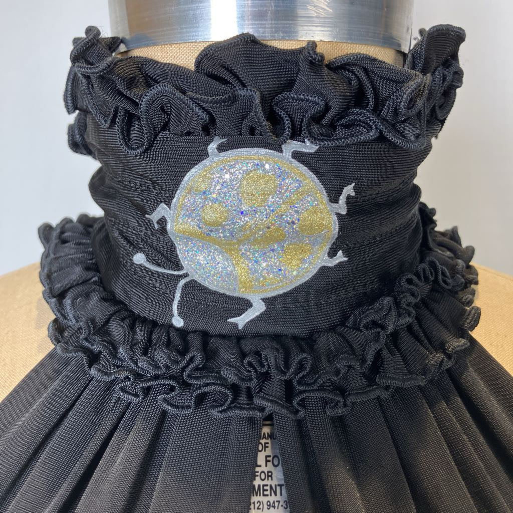Black ruffled dress with a gold and silver embroidered design on a mannequin.