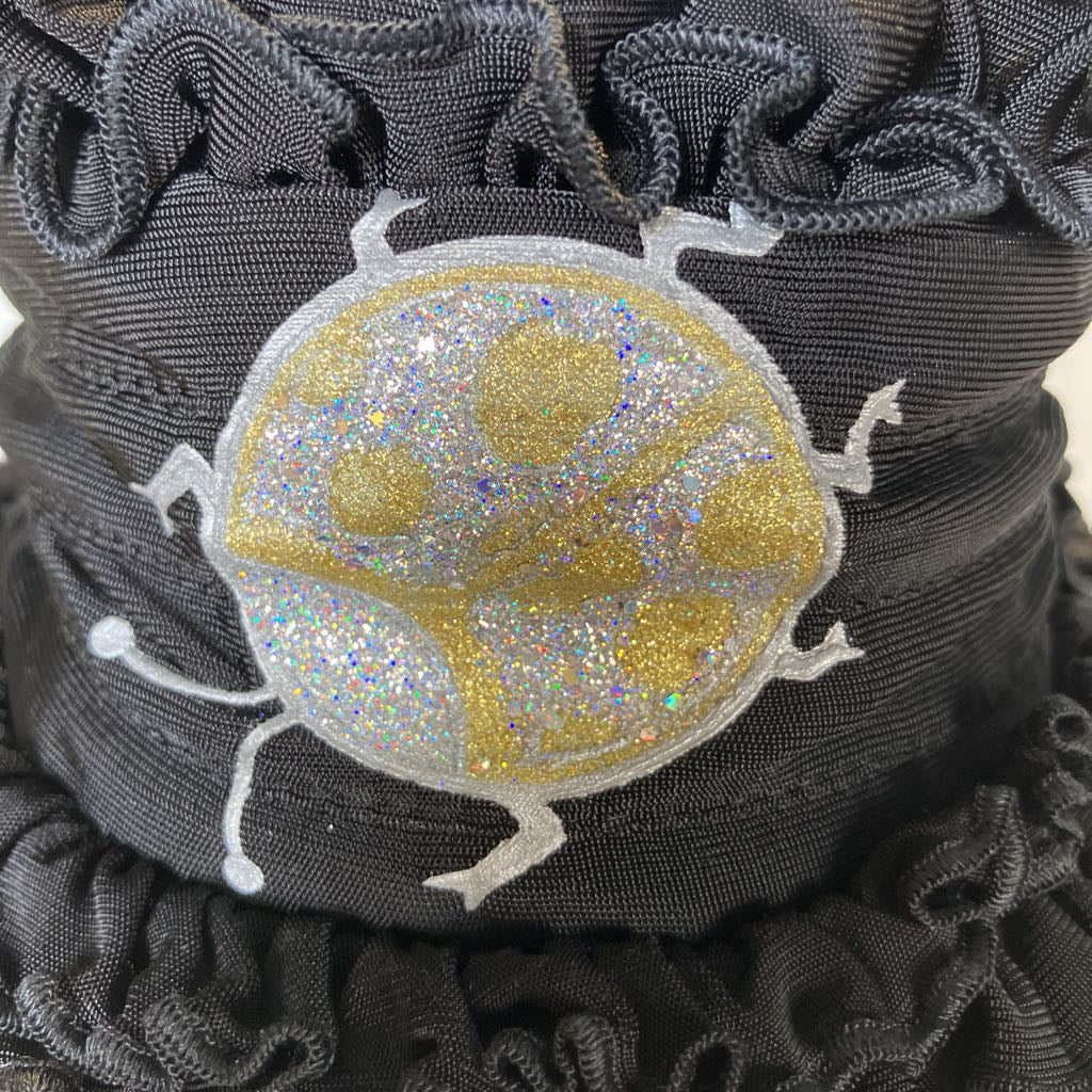 Close-up of a black scrunchie with a gold and silver embroidered design on a beige background