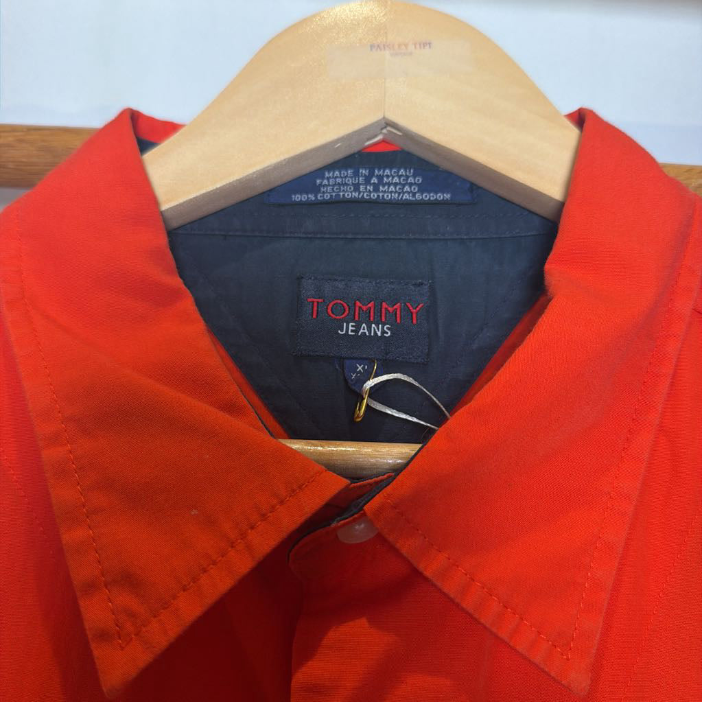 A close-up of a bright red Tommy Jeans button-up shirt hanging on a wooden hanger, showing the collar, inner neck lining, and brand label.