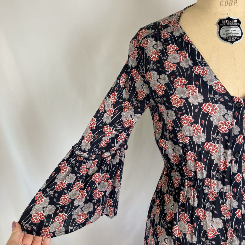 A navy blue long-sleeve blouse with a red and gray floral print, displayed on a beige dress form mannequin. The blouse features a V-neckline and a tiered ruffle sleeve.