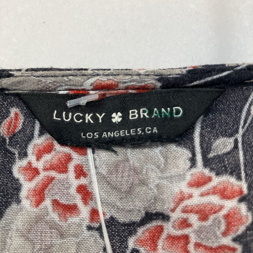 Close-up of a floral-patterned garment label reading 'LUCKY BRAND LOS ANGELES,CA' on a black fabric tag, with red, gray, and white floral print visible around it.