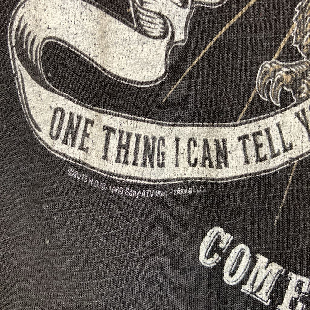 Close-up of a black graphic print featuring a white banner with the text 'ONE THING I CAN TELL' and part of a stylized illustration, with small copyright text reading '©2013 H-O© 1985 Sony/ATV Music Publishing LLC.'.
