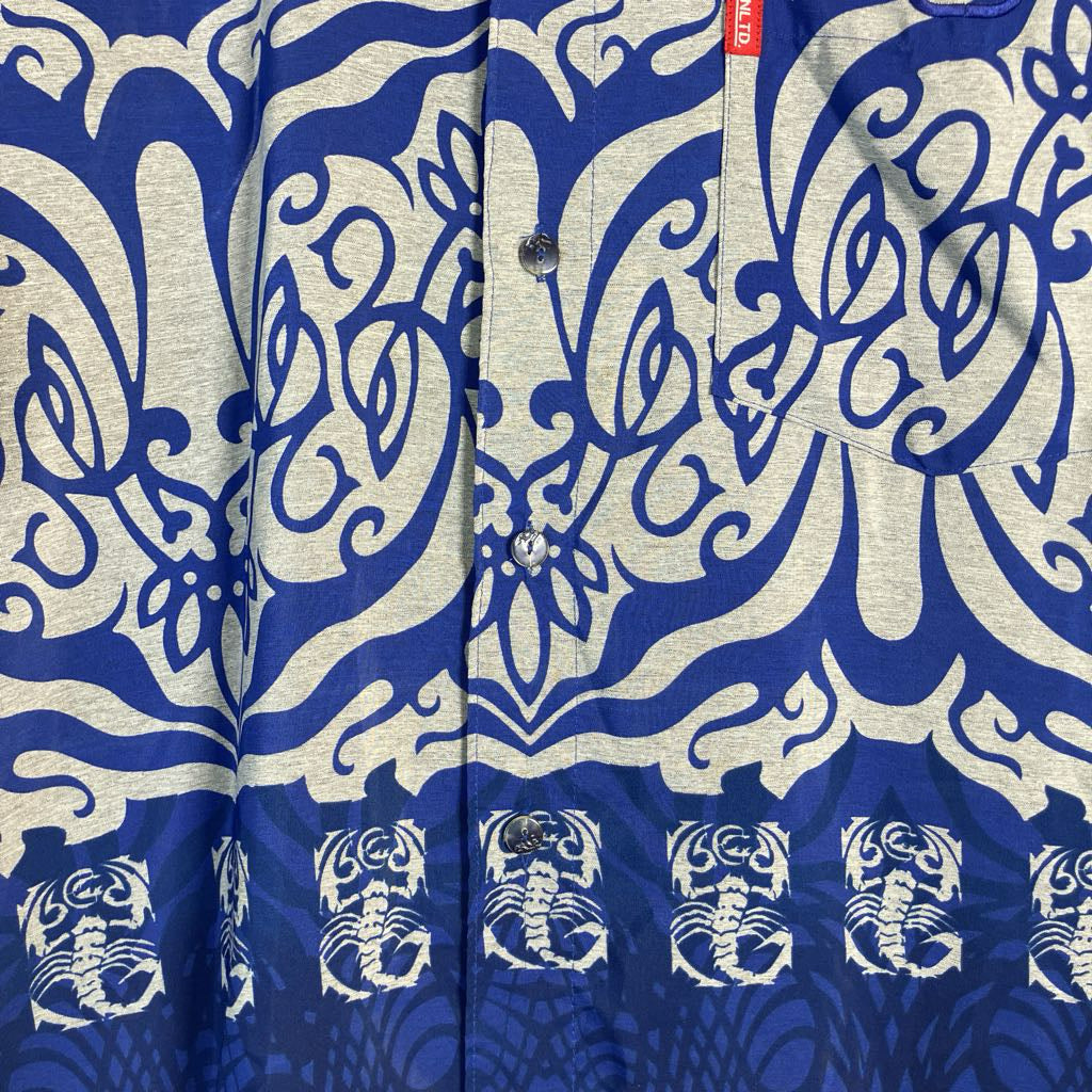 Close-up of a button-front shirt with a bold blue and off-white ornamental print and a row of white scorpion motifs along the lower front.