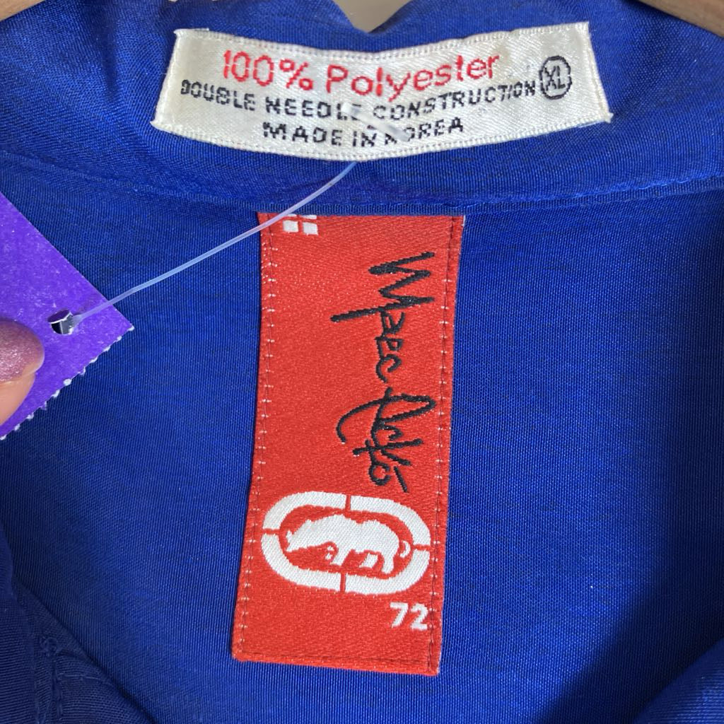 Close-up of a royal blue garment showing the inner neck labels, including a white '100% Polyester' tag and a red brand patch with black script and a white target logo.