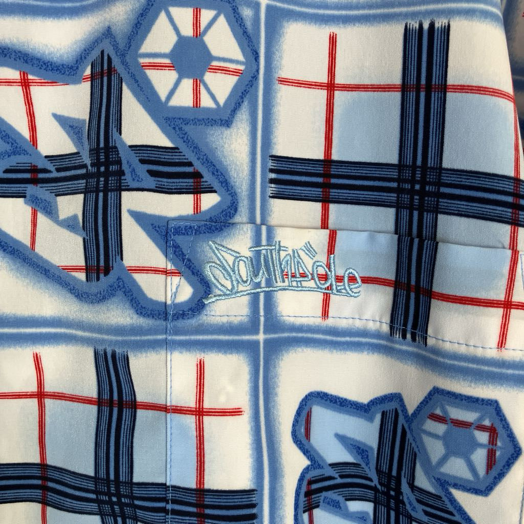 A close-up of a light blue and white patterned fabric with red grid lines, dark blue plaid sections, abstract blue shapes, and a central embroidered logo reading 'Southpole'.