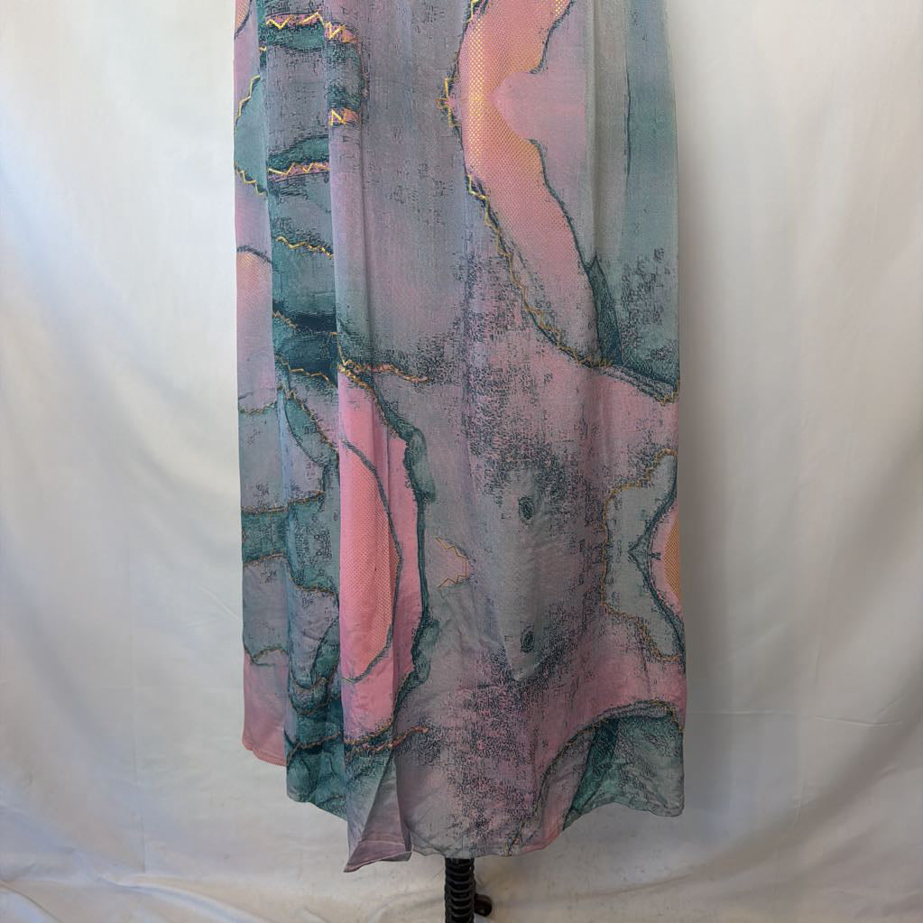 A long flowing skirt with an abstract marbled print in pastel pink, dusty blue, and gray, with thin metallic gold veining, hanging against a white fabric backdrop.