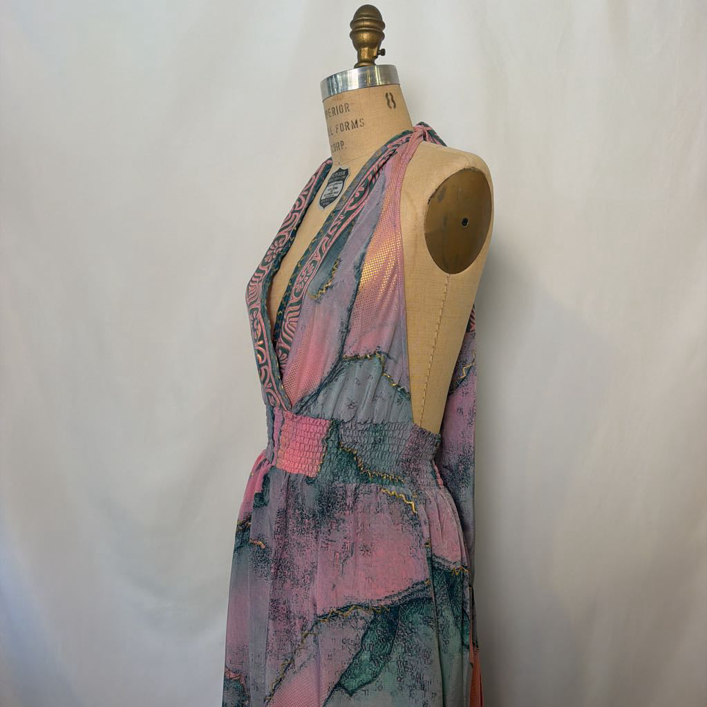 A sleeveless wrap-style dress displayed on a vintage wooden dress form mannequin against a light fabric backdrop. The dress features a multicolor abstract print with pink, teal, purple, and gray tones.