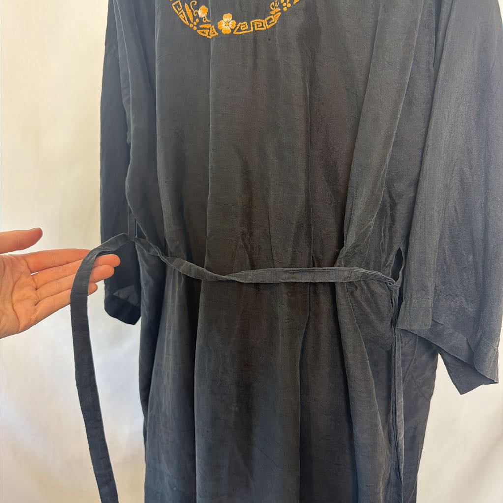 A dark charcoal gray wrap robe with a gold embroidered Greek key and floral pattern on the chest, held by a hand to show the waist tie.