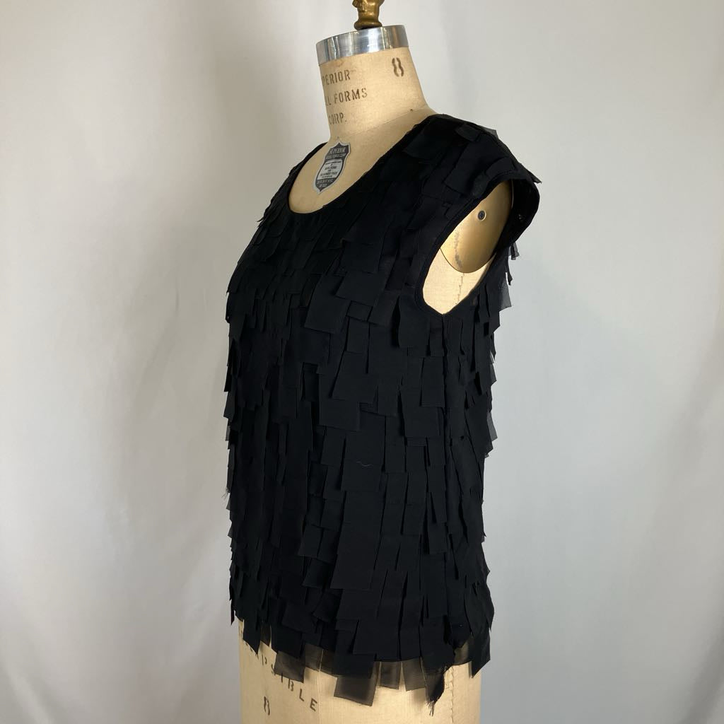 A sleeveless black fringed top displayed on a beige dress form mannequin against a light gray fabric backdrop.