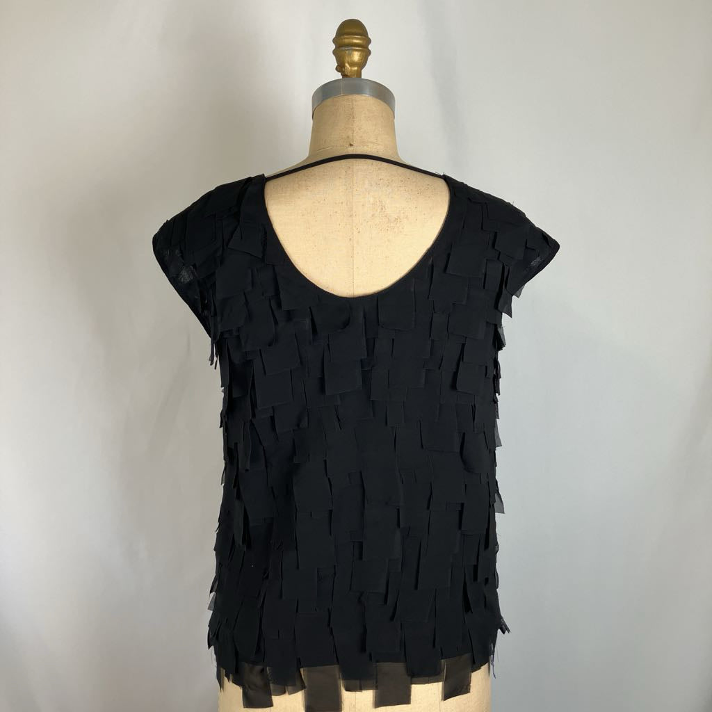 A black fringed top displayed on a dress form mannequin against a light gray background.