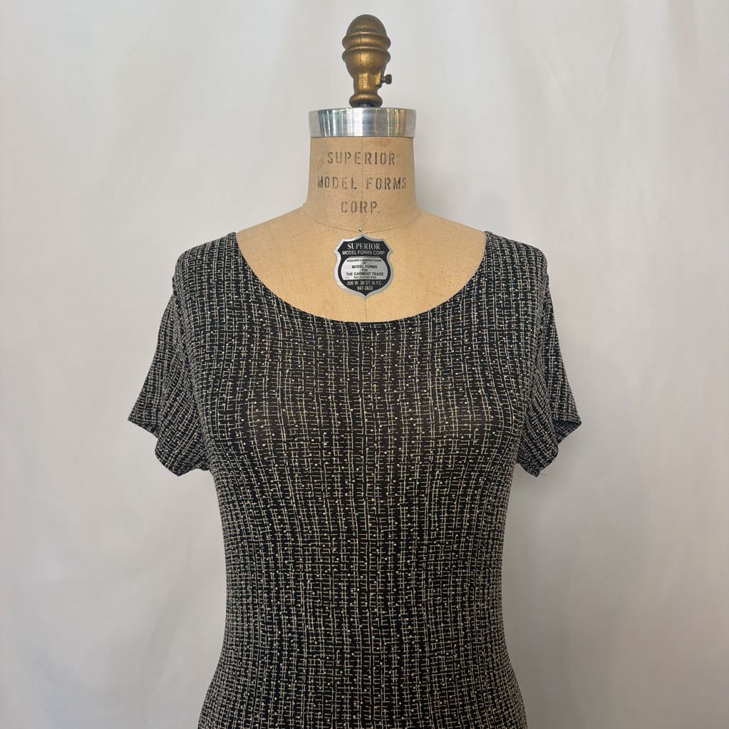 A short-sleeve scoop-neck knit top in a black and white textured tweed pattern, displayed on a vintage tan mannequin dress form against a light gray fabric backdrop.