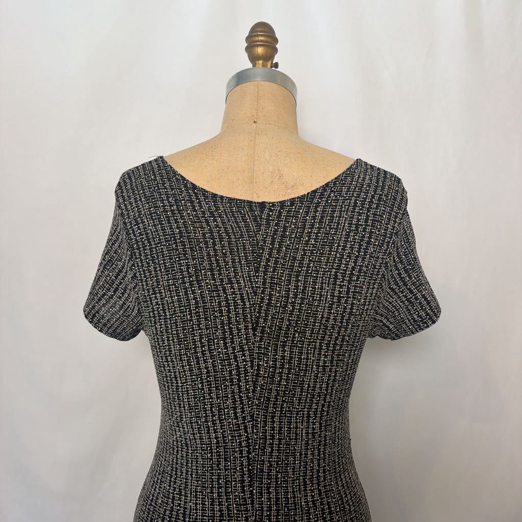 A short-sleeve knit top displayed on a dress form mannequin against a plain light background. The top features a textured, ribbed pattern in black and white threads, creating a gray appearance, with a wide boat neckline.