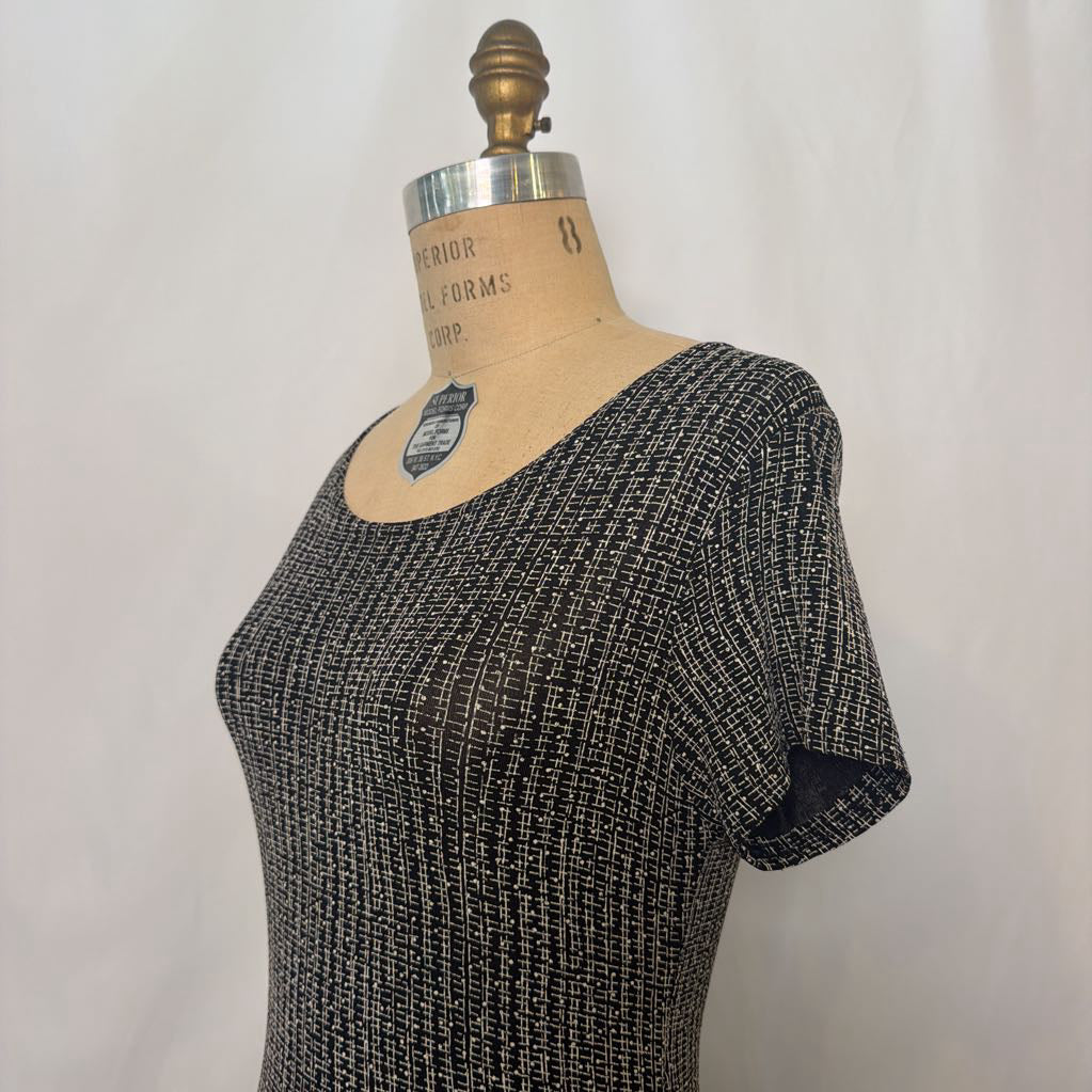 A short-sleeve scoop-neck knit top in a black and white heathered textured fabric, displayed on a vintage wooden dress form mannequin against a light gray fabric backdrop.