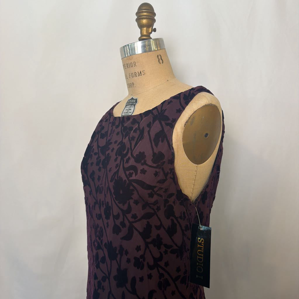 A sleeveless scoop-neck dress displayed on a vintage wooden dress form mannequin. The dress features a dark purple base with a black floral vine pattern.
