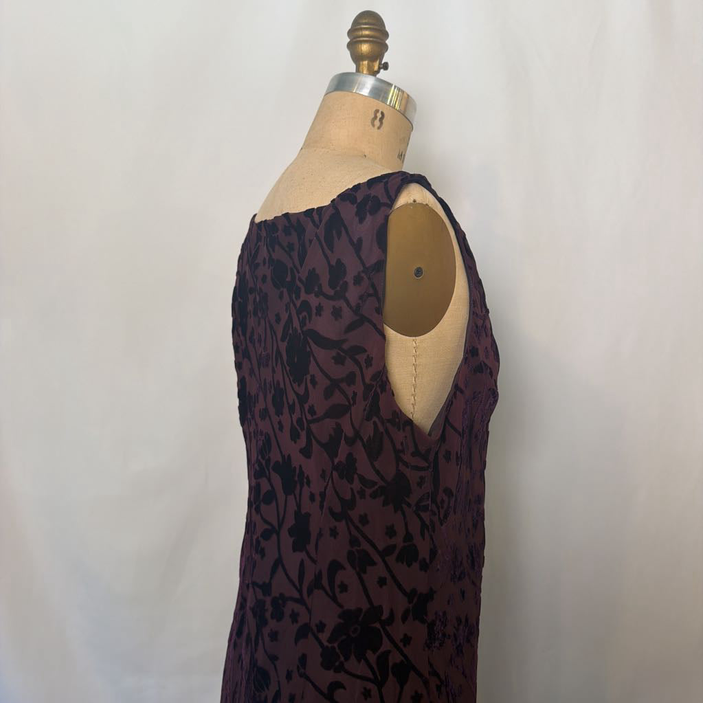 A sleeveless dark plum dress with a black floral pattern, displayed on a beige dress form mannequin against a white fabric backdrop.