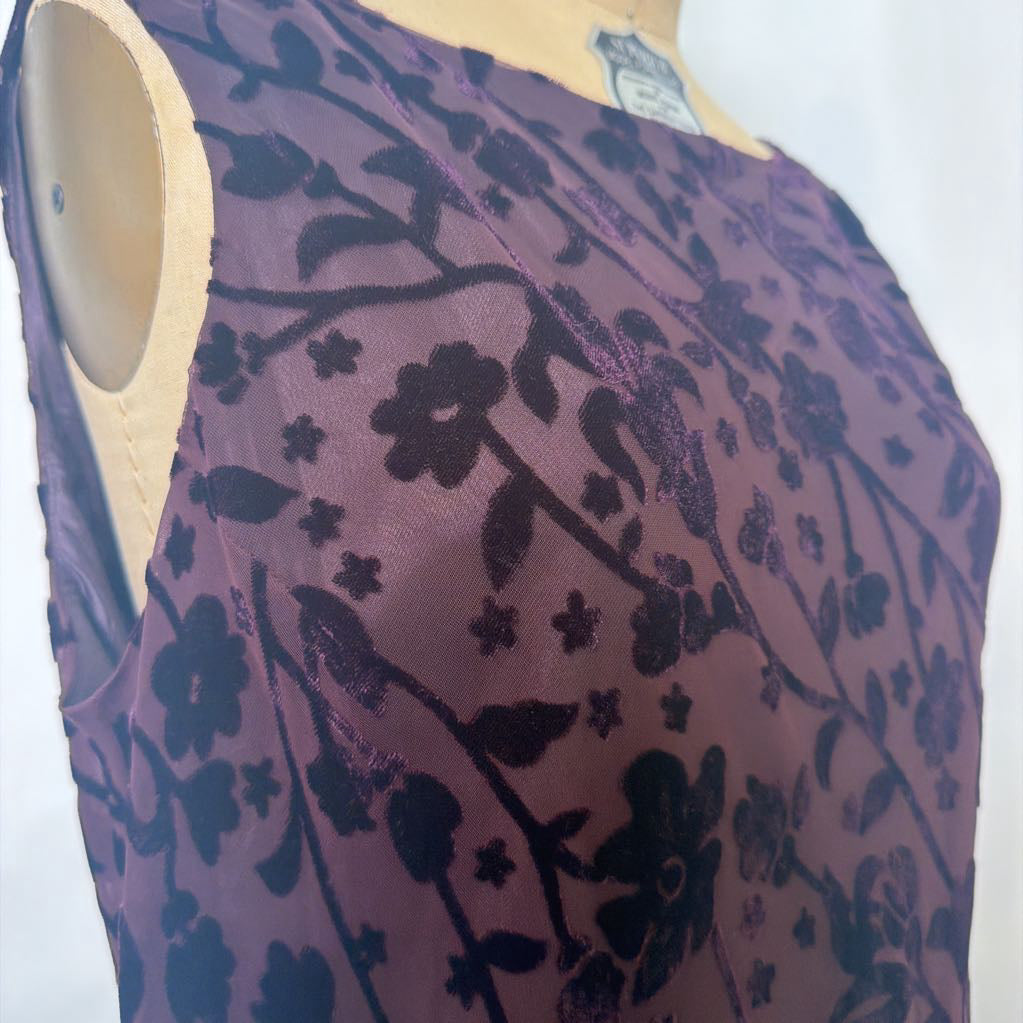 A sleeveless sheer purple top with a black floral and vine pattern, displayed on a beige dress form against a white background.