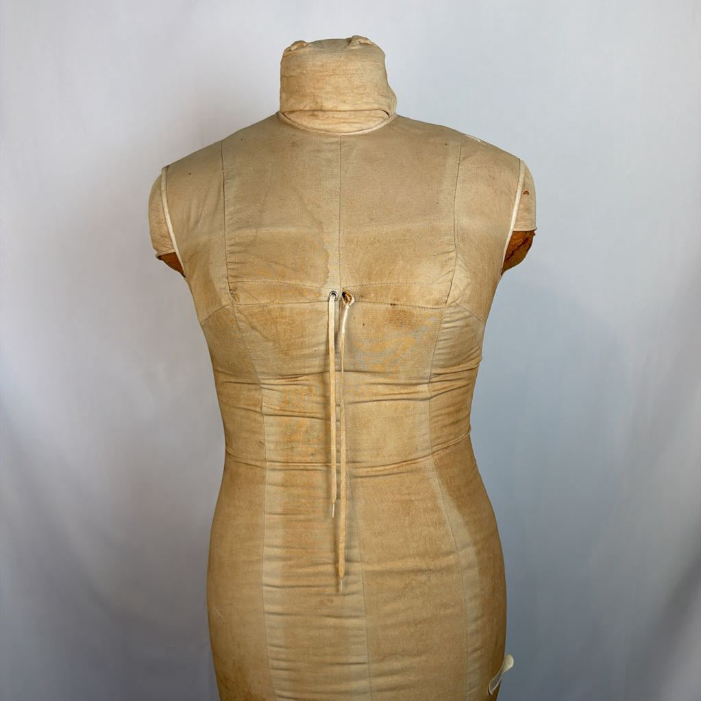 A beige sleeveless dress form or mannequin torso with a high mock neck, photographed against a plain light gray backdrop.