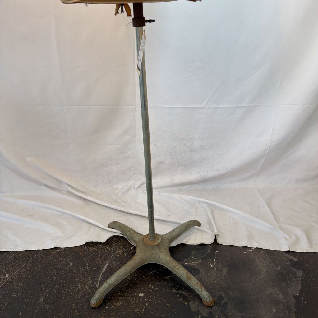 A vintage metal music stand with a five-star base and a silver vertical stand, photographed against a draped white fabric backdrop.