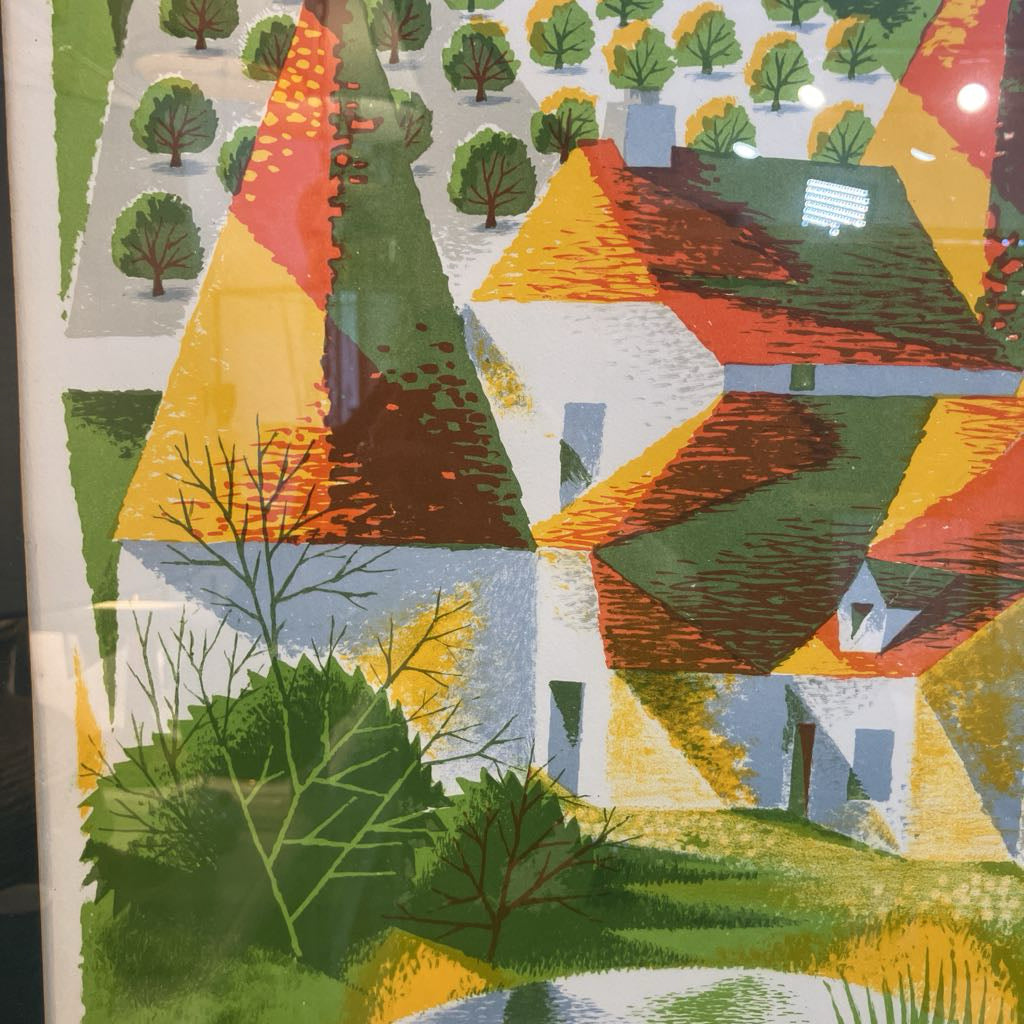 A colorful geometric landscape art print depicting houses with red roofs, green trees, and yellow fields, shown with a white border and visible reflections on a glossy surface.
