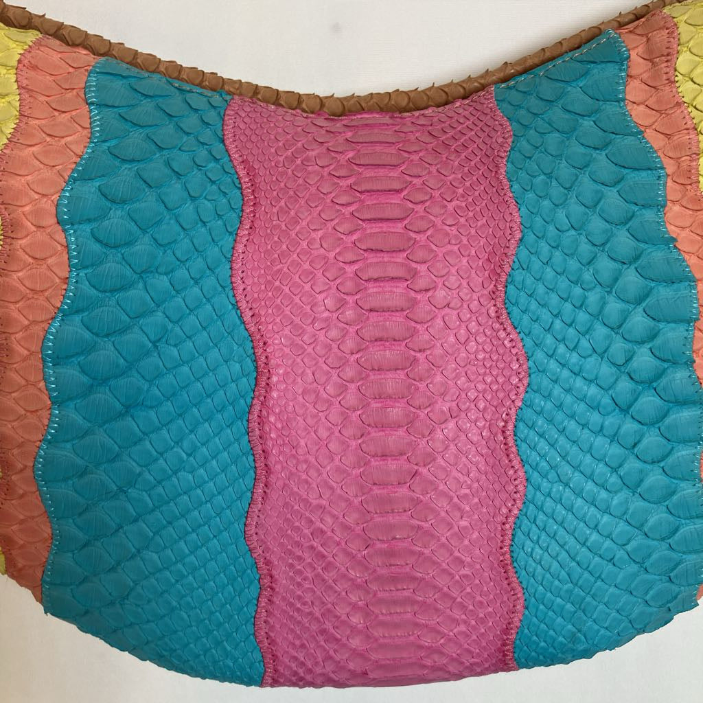 A close-up of a colorful leather panel with vertical wavy stripes. The center stripe is pink with a reptile-like texture, flanked by teal-blue, peach, and yellow textured sections, finished with a brown braided trim at the top.