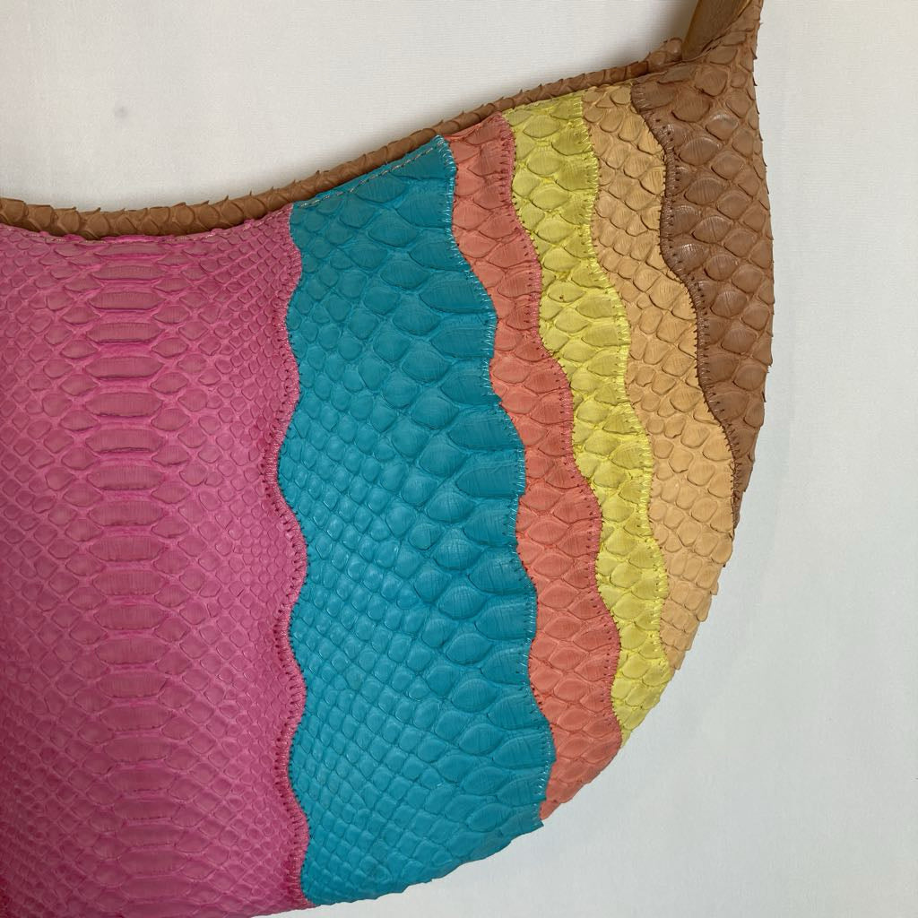 A close-up of a multicolor quilted leather shoulder bag with wavy vertical stripes in pink, teal, coral, yellow, and brown, featuring a textured scale pattern and a tan woven strap.