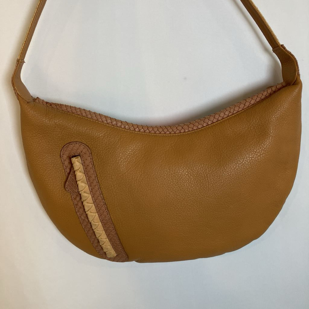 A tan pebbled leather crescent-shaped shoulder bag with a braided trim detail on the front pocket and strap, shown against a plain white background.